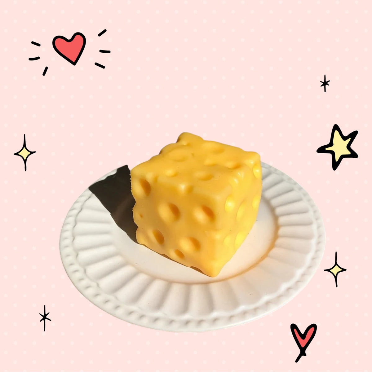 Foundry FitFit yellow cheese block squishy fidget toy on a small white plate with a playful pink background