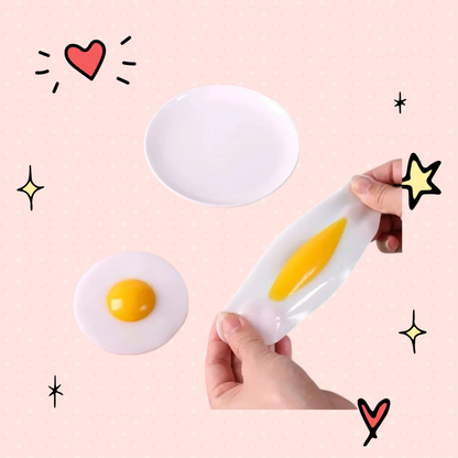 Foundry FitFit egg-shaped squishy fidget toy being stretched by hand next to a plate on a pink and green background