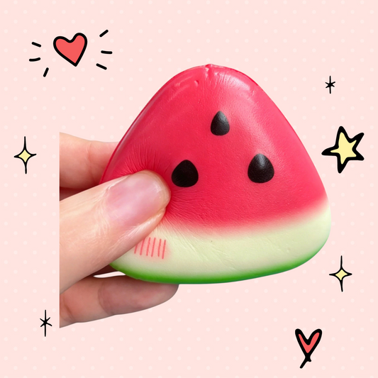 Foundry FitFit squishy watermelon fidget toy made of soft latex, held in hand against a blue wooden background with flowers