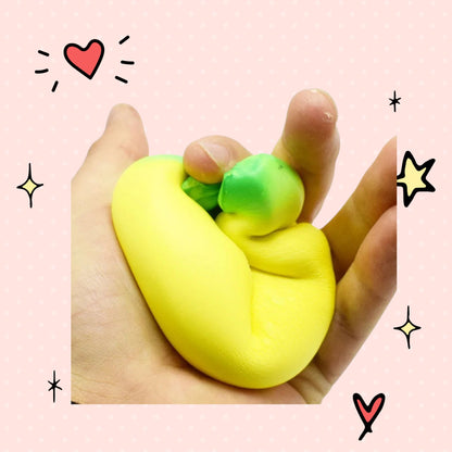 Foundry FitFit jumbo yellow banana slow-rise foam squishy toy being squeezed in a hand against a pink background