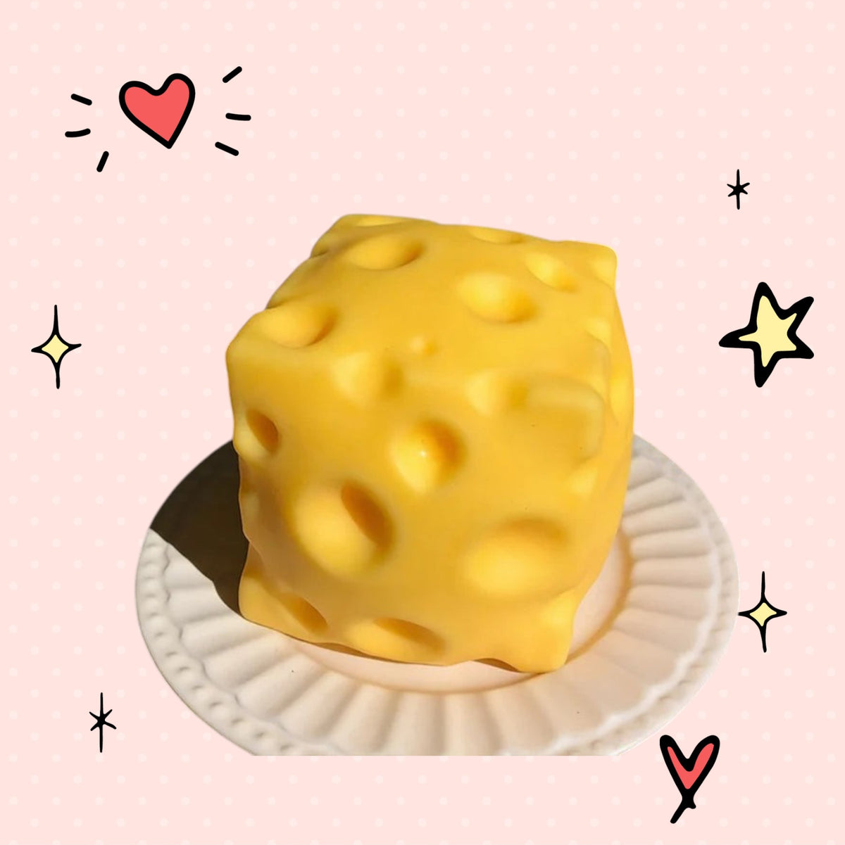 Foundry FitFit yellow cheese block squishy fidget toy on a small white plate against a pink dotted background.