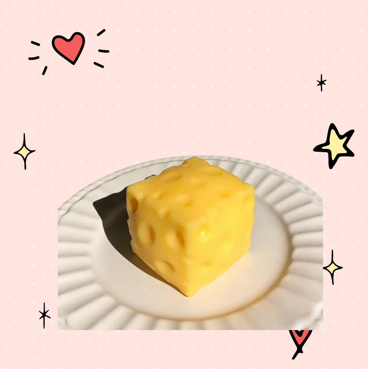 Foundry FitFit yellow cheese block squishy fidget toy on a white plate against a pink background with doodle stars.