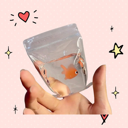 Foundry FitFit orange goldfish squishy toy inside a clear plastic bag held in a hand against a pink background