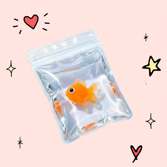 Foundry FitFit orange goldfish squishy toy inside a clear plastic bag on a pink background with doodle stars and hearts