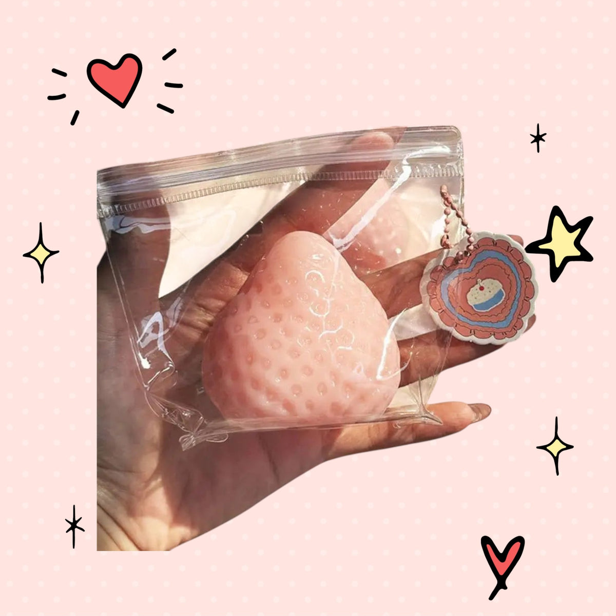 Foundry FitFit pink strawberry squishy fidget toy in a clear plastic bag with a heart-shaped tag held in a hand.